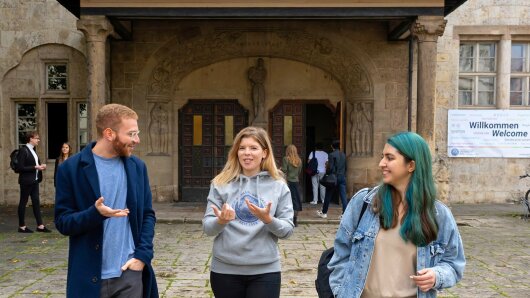Studierende kommen fröhlich diskutierend aus dem Universitätshauptgebäude