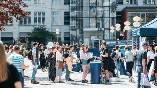 eine Reihe von Menschen vor dem Informationsstand der Abteilung Hochschulkommunikation auf dem Campus
