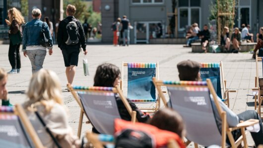 Besuchende sitzen auf Liegestühlen des Uni-Shops auf dem Campus zum Hochschulinformationstag