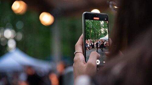 Person schaut durch die Handykamera auf eine Veranstaltung