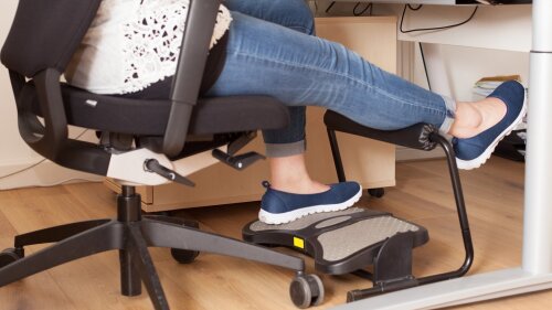 Mitarbeiterin mit ergonomischer Fußstütze unter dem Schreibtisch