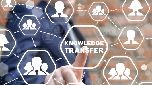 Ein Finger tippt auf das Icon "Knowledge Transfer", dieses ist umgeben von einem Netzwerk an Personen-Icons.