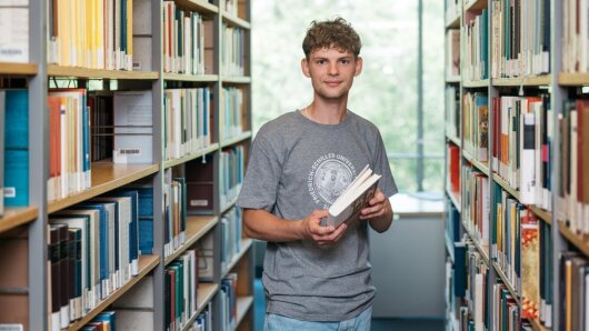 Person steht vor Bücherregal und hält Buch in der Hand