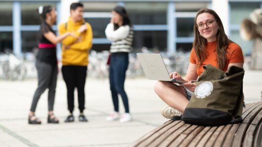 Person sitzt auf dem Campus mit einem Laptop auf dem Schoß
