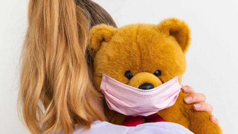 Ein Teddybär mit einer Mundschutzmaske wird auf dem Arm gehalten
