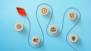 Rotes Papierboot navigiert durch Holzklötzer mit Icons auf blauem Hintergrund