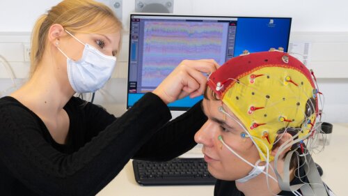 A woman puts an EEG cap on a person.