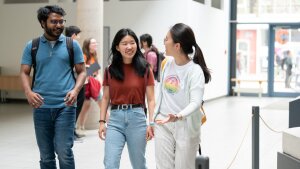 Three students walk through the lecture hall building and talk to each other