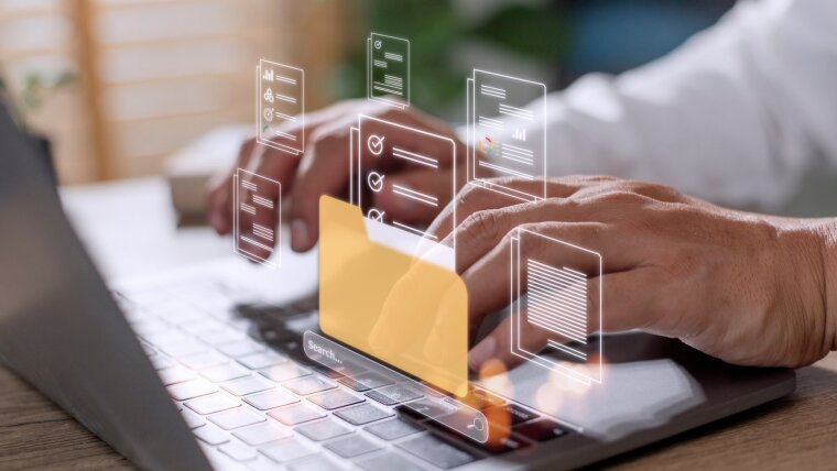 Finger tippen auf einer Laptop-Tastatur. Über der Tastatur sind Hologramme von Ordnern und Dokumenten zu sehen.