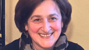 Portrait der lächelnden Frau Prof. Dr. Ekaterine Shaverdashvili. Sie trägt einen grau-schwarz gemusterten Schal und steht vor einer beigen Wand.