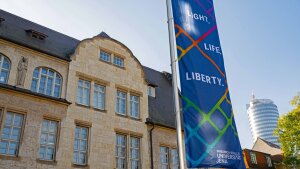A flag bearing the motto »Light.Life.Liberty.« can be seen in front of the main building of the University of Jena.