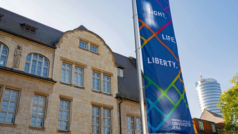 Vor dem Hauptgebäude der Universität Jena ist eine Flagge zu sehen mit dem Motto »Light.Life.Liberty.«