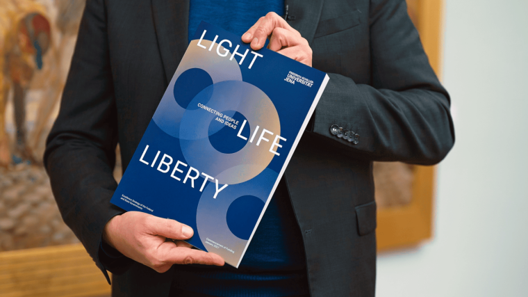 Universitätspräsident Prof. Dr. Andreas Marx hält ein Exemplar des Exzellenzantrags in der Hand