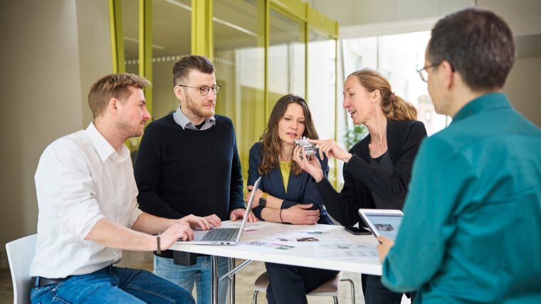 Five researchers have gathered around a table and are discussing a redox flow battery.