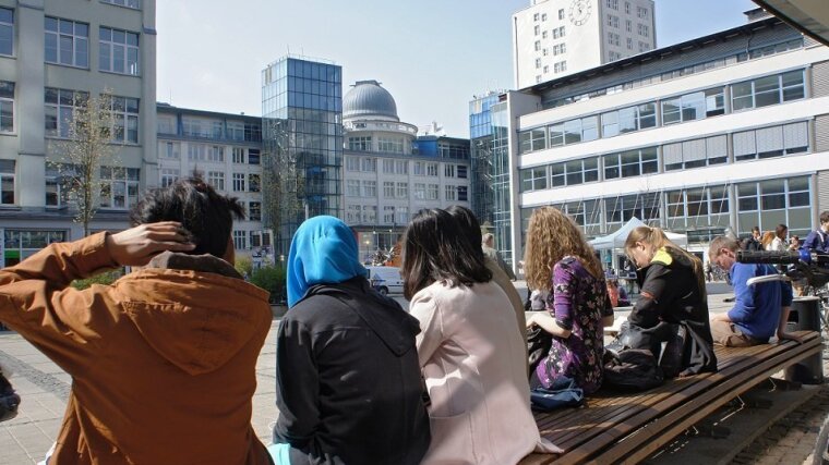 Studierende sitzen auf einer Bank am Campus