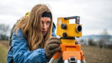 A young woman looks through a measuring device to collect geophysical data in the field