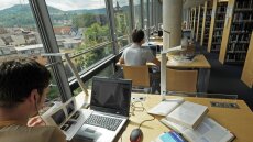 Young man working at a reading desk in the library in front of large windows with view over Jena