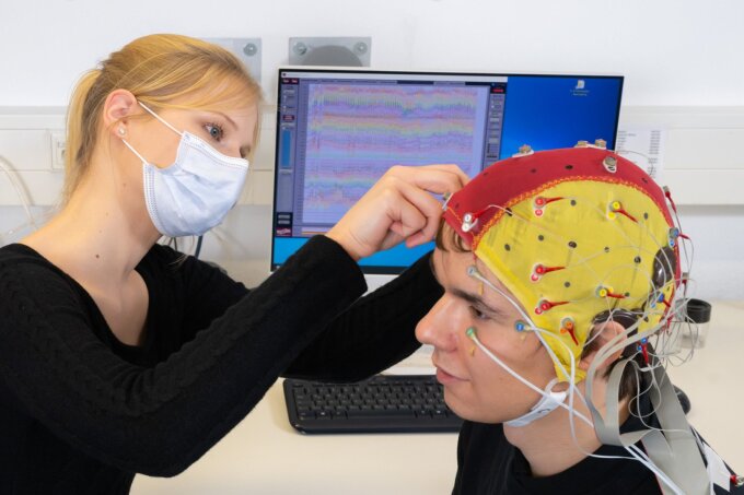 Doktorandin Celina von Eiff befestigt Elektroden an einer Kappe, die der Proband Lucas Riedel während einer EEG-Studie mit Cochlea-Implantaten trägt.