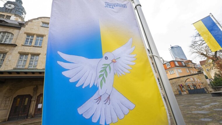 Eine Fahne mit den Nationalfarben der Ukraine und dem Abbild einer Friedenstaube weht vor dem Universitätshauptgebäude.