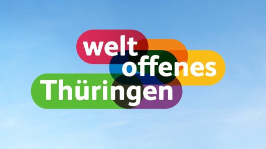 Der Claim »weltoffenes Thüringen« steht als buntes Logo vor blauem Himmel.
