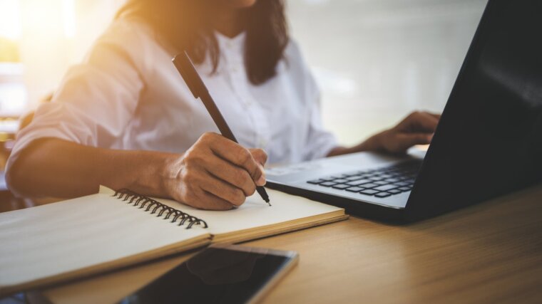 Eine Person am Laptop, die sich per Hand Notizen macht