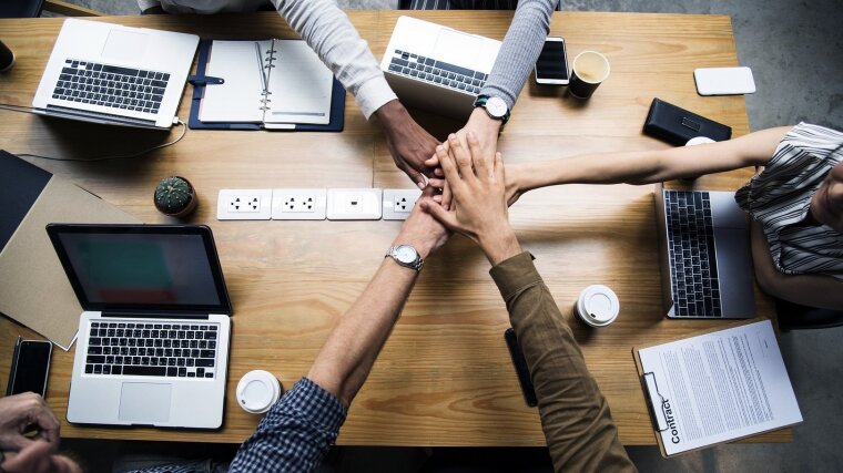 Five hands crossed over a meeting table.