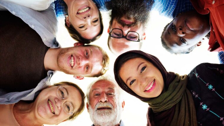 Photograph of people of different ages, cultures, and origins standing in a circle looking down at the camera