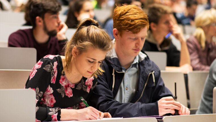 filled lecture hall with two students in the foreground