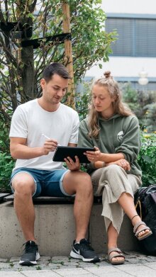 Zwei Studierende sitzen und arbeiten mit einem Tablet